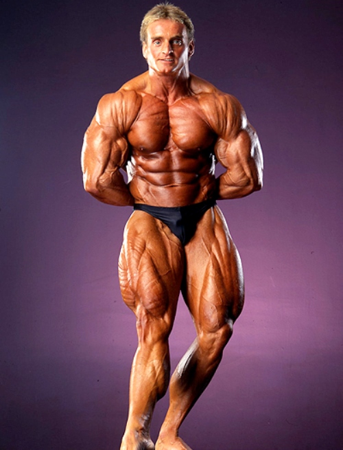 Andreas Munzer flexing his muscles for a photo, looking ripped and muscular
