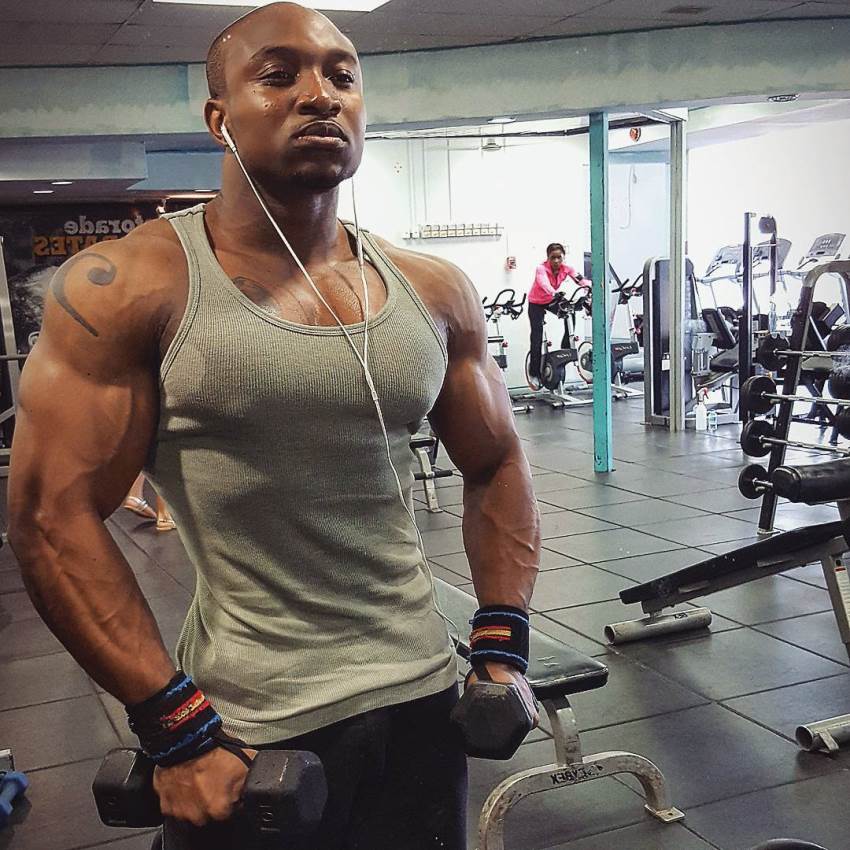 Antonio Mitchell showing his ripped physique in a grey tank top in the gym