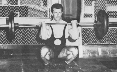 Bob Gajda in a squat position with a weighted barbell over his shoulders, preparing to do a movement