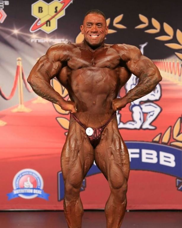 Darryn Onekawa doing a front lat spread on the bodybuilding stage in front of the audience