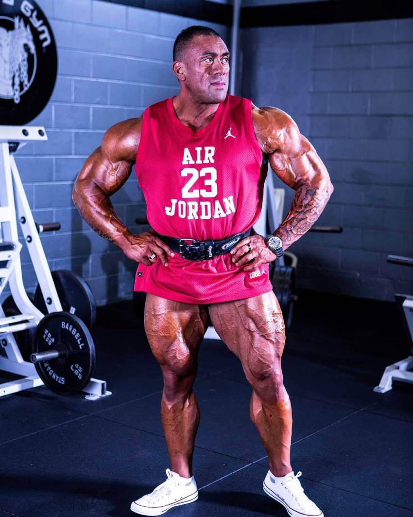 Darryn Onekawa standing in the gym in red tank top, looking ripped and big