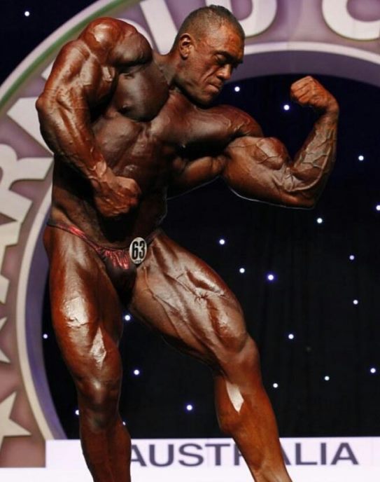 Darryn Onekawa flexing his biceps on the bodybuilding stage