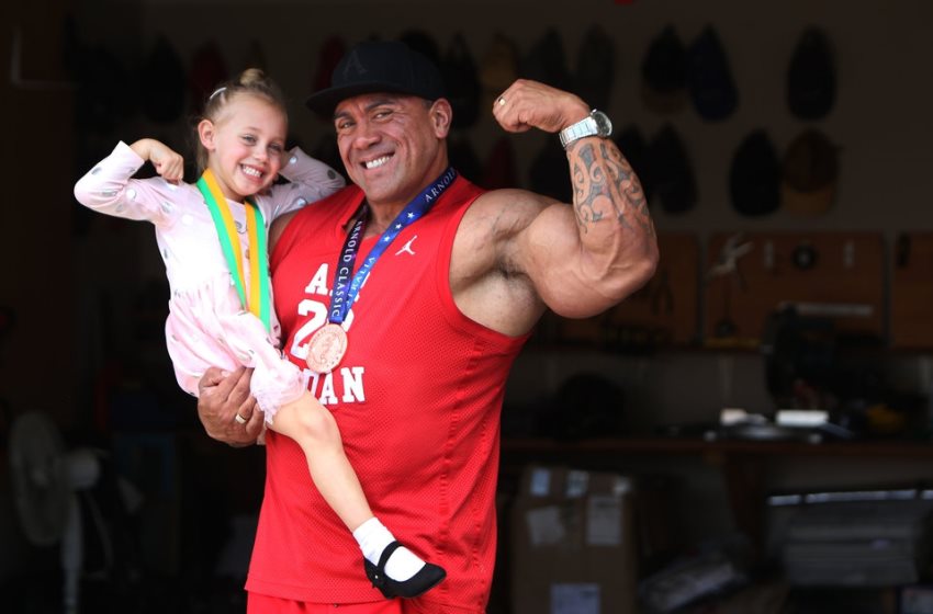 Darryn Onekawa flexing his biceps while holding his daughter