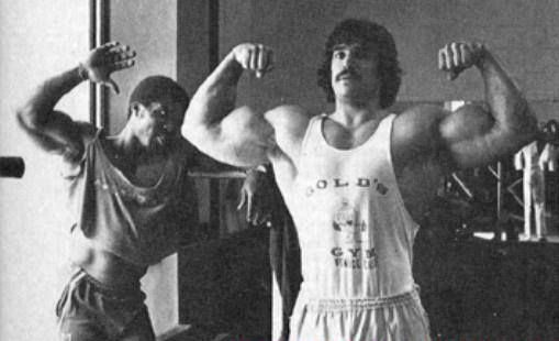 Denny Gable doing a front double biceps flex with Robby Robinson behind him posing