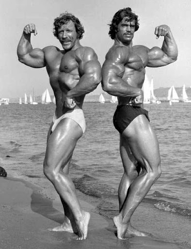 Denny Gable on the right, flexing his biceps on the beach with Kent Kuehn