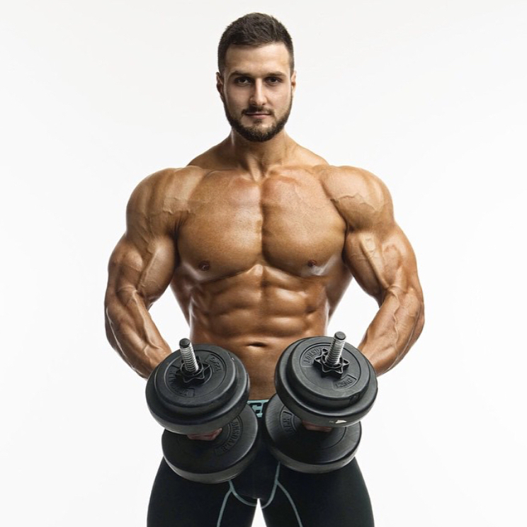 Emil Goliath posing shirtless with two dumbbells in his hands, looking muscular