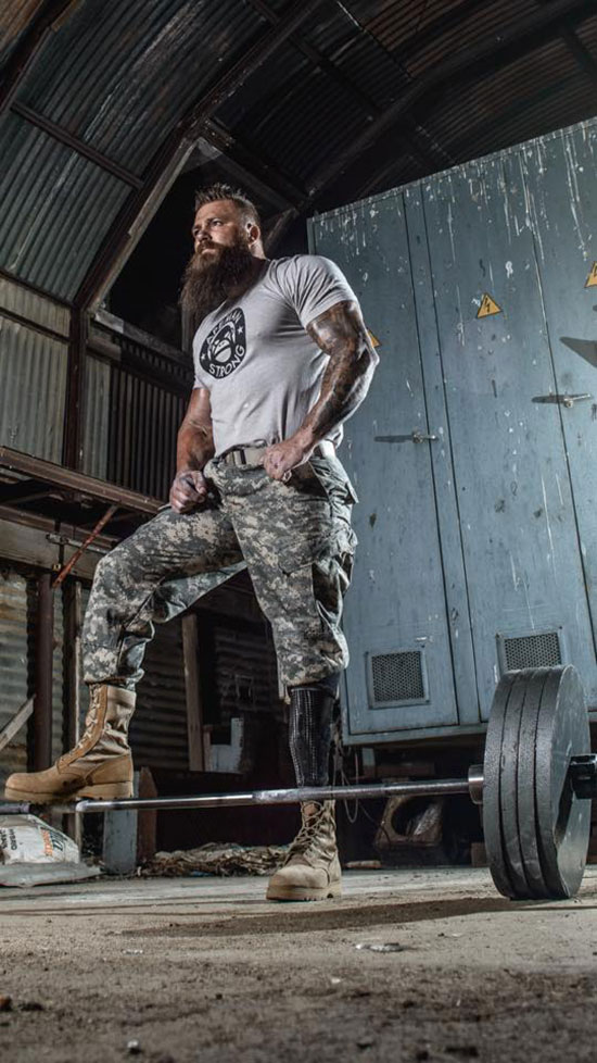 KC Mitchell stood with his foot on a barbell with is army gear on.