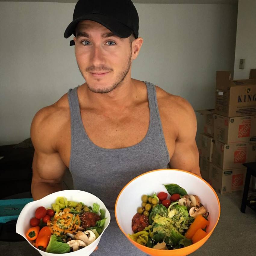 Nimai Delgado wearing a grey tank top and showing his vegan meals to the camera