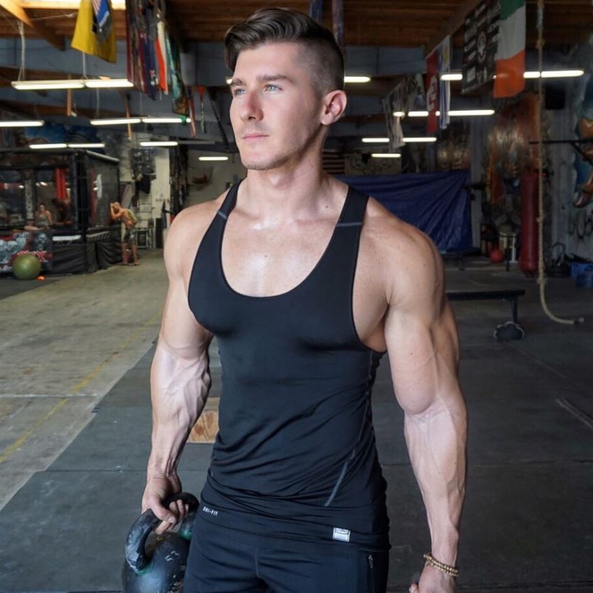 Nimai Delgado standing in the gym posing for a photo in black tank top, looking ripped