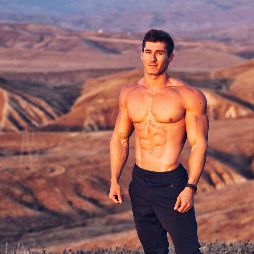 Nimai Delgado standing shirtless on top of a red canyon, looking lean and muscular