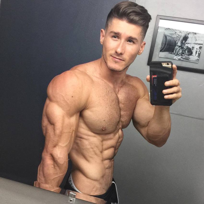 Nimai Delgado taking a selfie of his flexed triceps and obliques in a mirror