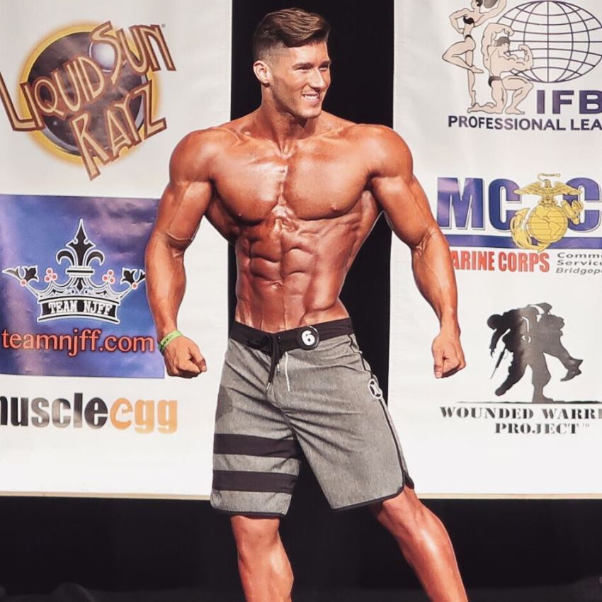 Nimai Delgado on a Men's Physique stage looking ripped and muscular