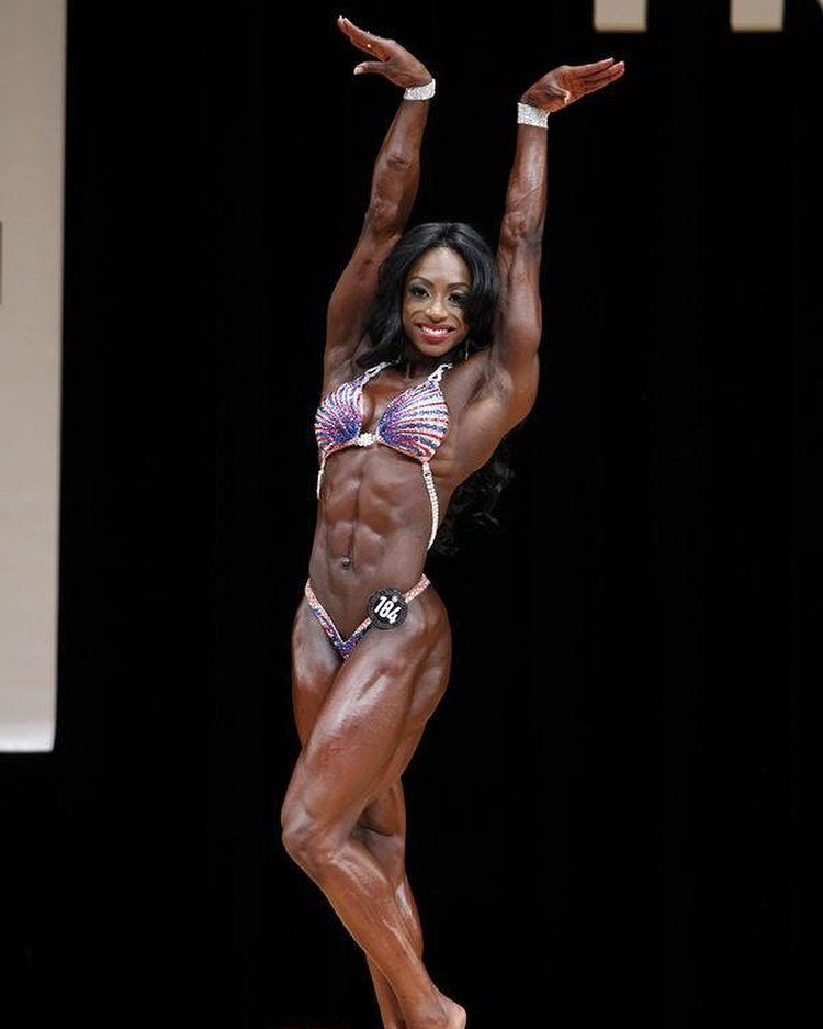 Shanique Grant posing on stage at a bodybuilding show.
