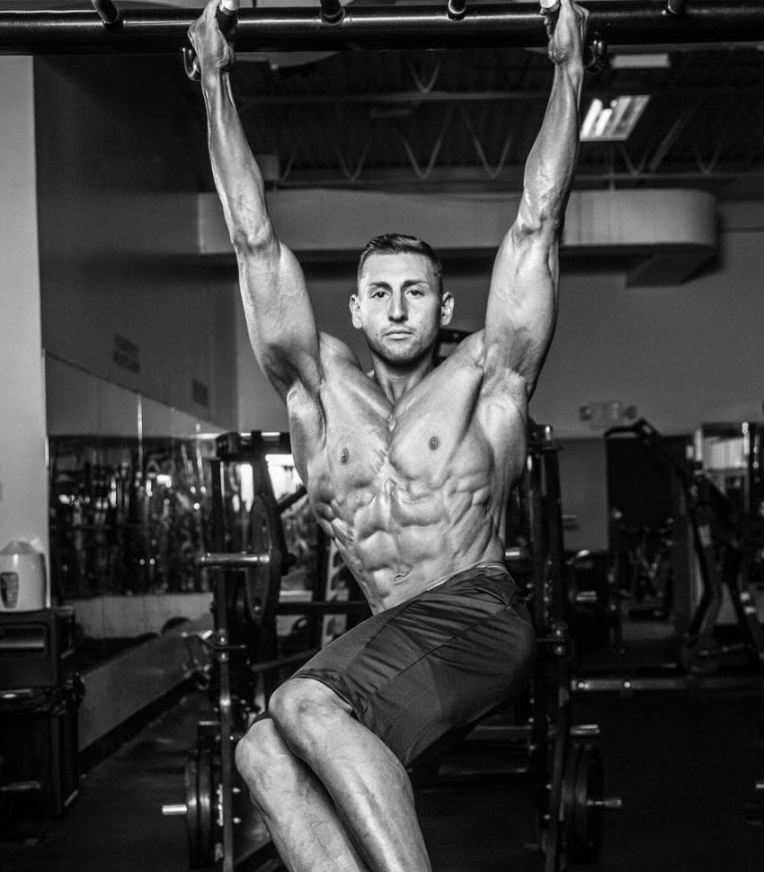 Anthony Scalza doing shirtless hanging leg raises, looking ripped and aesthetic