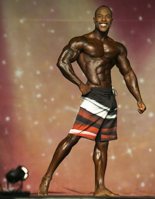 Antoine WIlliams doing a side pose on Men's Physique bodybuilding stage