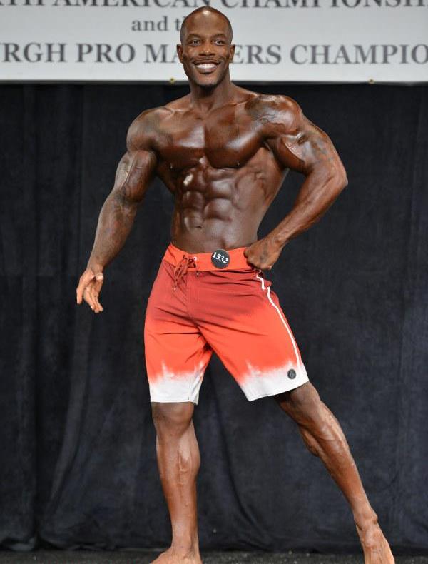 Antoine Williams smiling at the judges and showing off his muscular physique on the men's physique stage