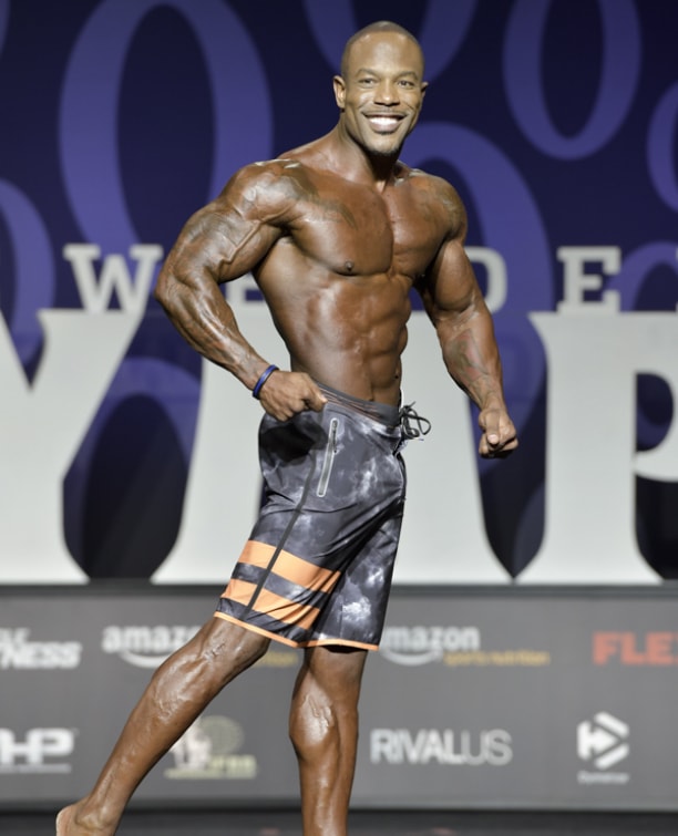 Antoine Williams smiling at the Men's Physique Olympia stage, looking ripped and muscular