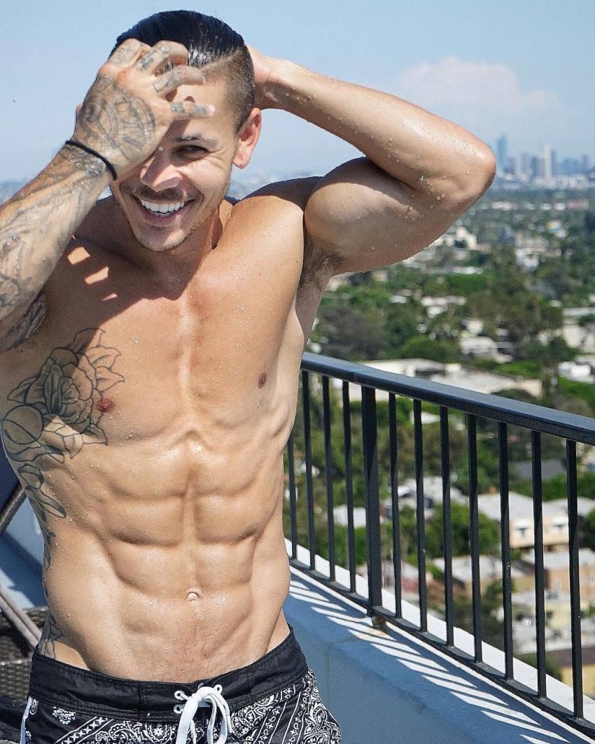 Brandon Schram standing shirtless on a balcony smiling for a photo, looking ripped