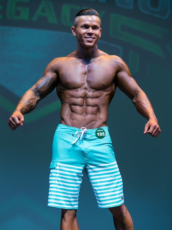 Brandon Schram posing on the Men's Physique bodybuilding stage looking ripped and muscular