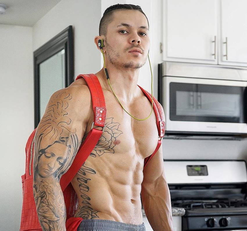 Brandon Schram wearing a red backpack while being shirtless, looking fit and ripped