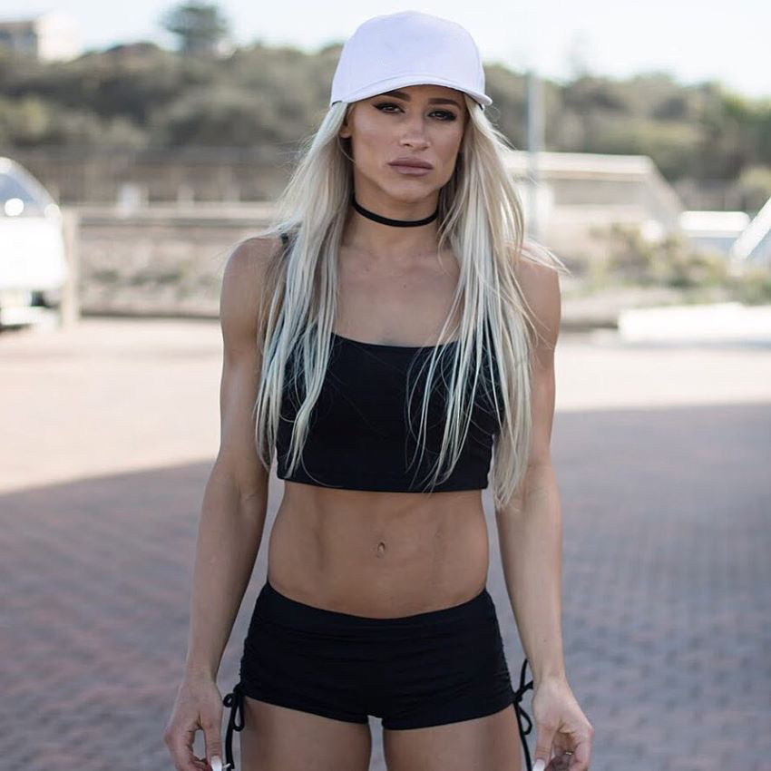 Christine Ray looking straight at the camera, showing her lean and fit body in black sports outfit