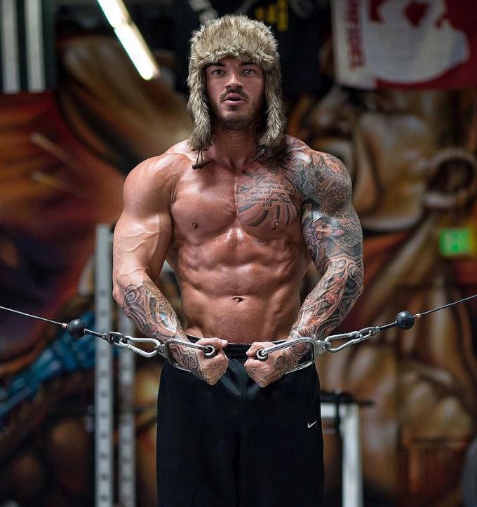 Devin Physique doing cable crossovers in the gym while being shirtless, wearing a winter hat