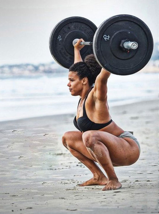 Elizabeth Akinwale training with a barbell on the beach.