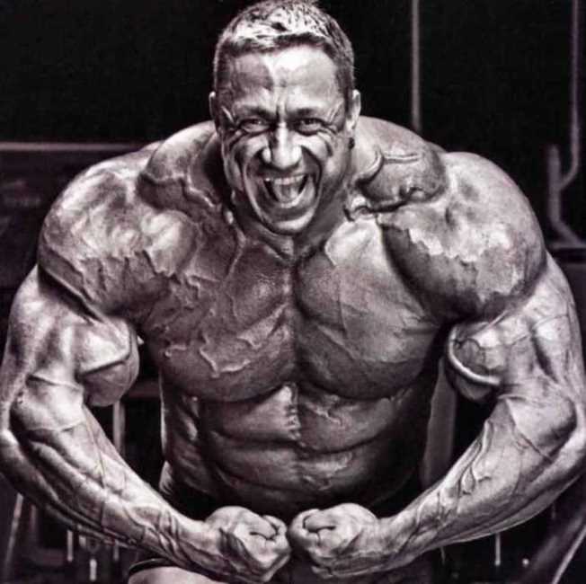 Markus Ruhl looking straight at the camera while doing a most muscular pose, looking incredibly massive and ripped