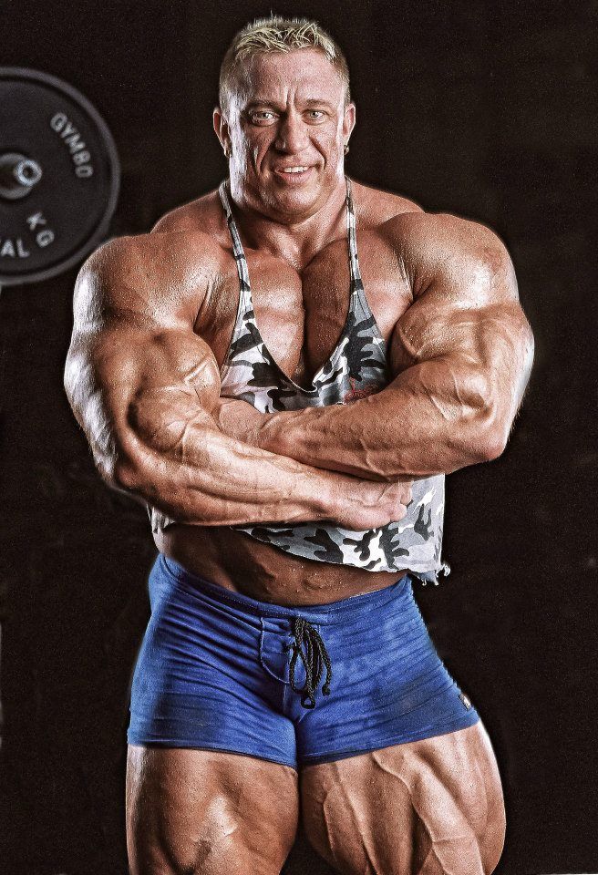Markus Ruhl with his arms crossed in a camouflaged tank top, looking massive and ripped