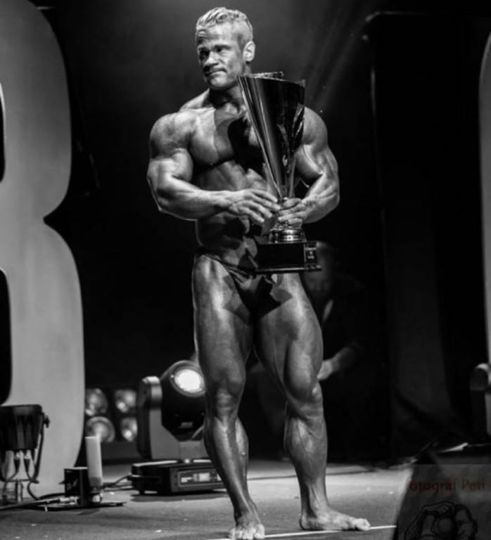 Nicolas Vullioud standing on the bodybuilding stage with a trophy in his arms