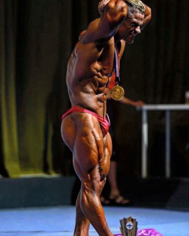 Side shot of Nicolas Vullioud flexing his abs and legs on the bodybuilding stage