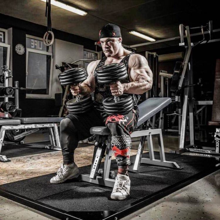 Nicolas Vullioud sitting on a gym bench and holding two dumbbells, preparing to do an incline chest press