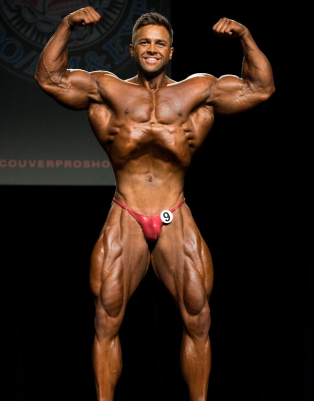 Regan Grimes flexing his biceps on the bodybuilding stage, looking conditioned and muscular