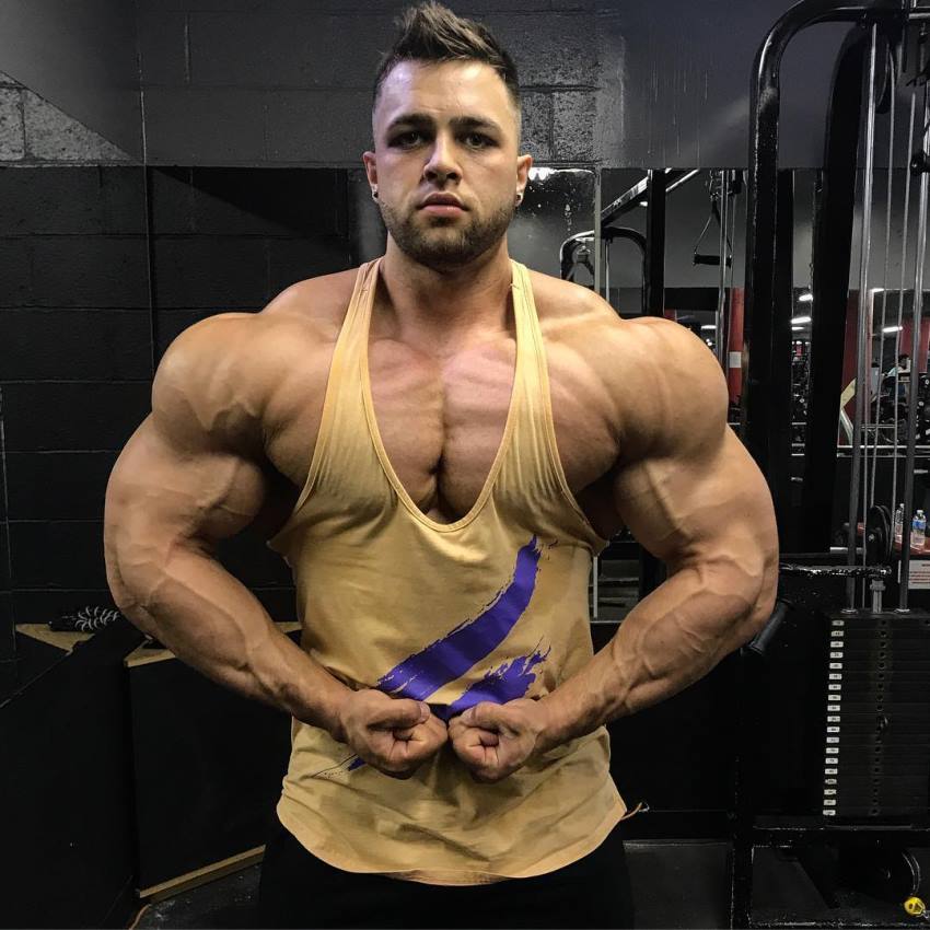 Regan Grimes flexing his arms and shoulders in a yellow tank top