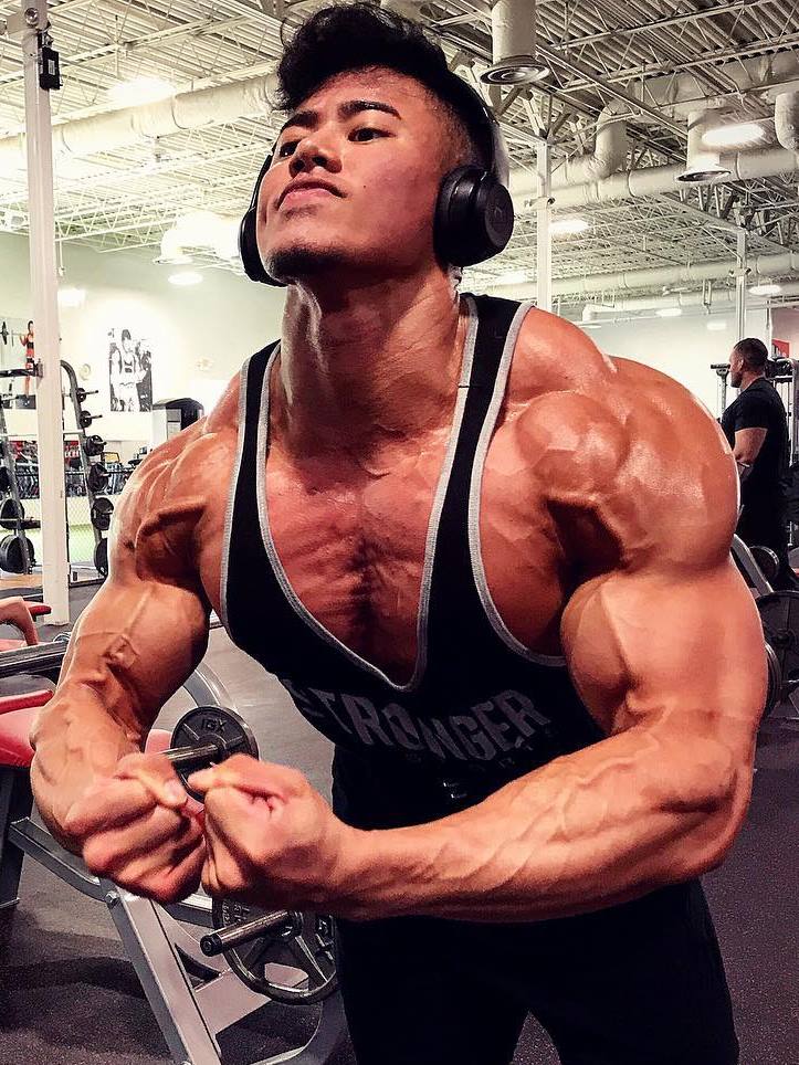 Steven Cao wearing black tank top, flexing in the gym