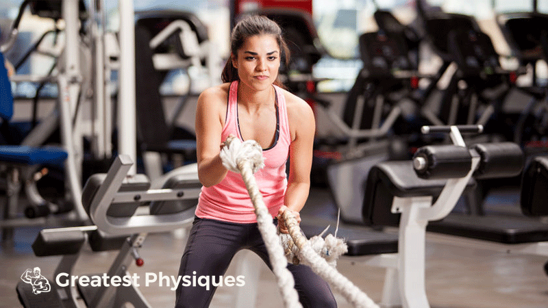 Female athlete in pink sportswear using battle ropes in the gym