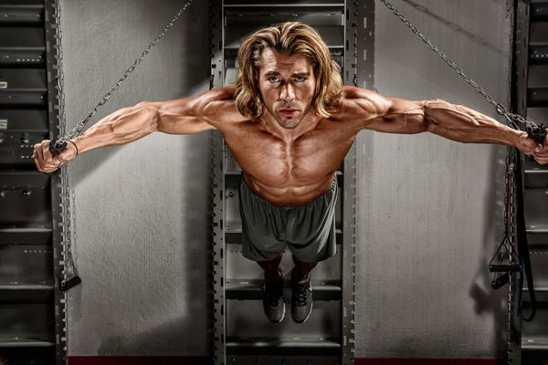 Craig Capurso in a photo shoot holding his weight with cables.