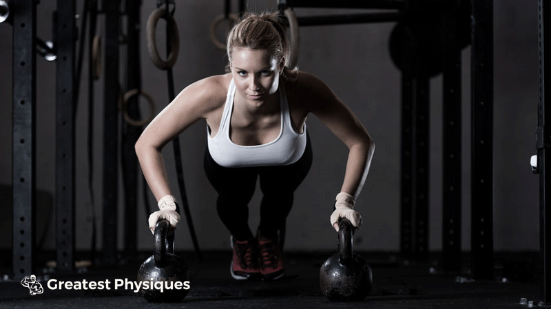 Young, athletic female performing push-ups on kettlebells in the gym
