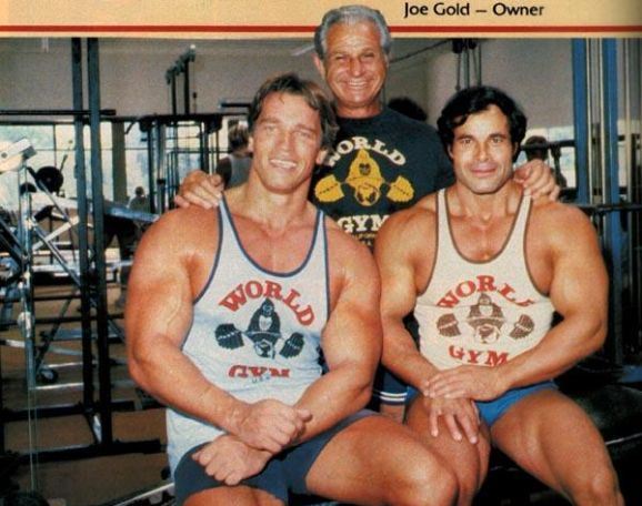 Joe Gold posing for a photo with two bodybuilders in his gym, one of them is Arnold Schwarzenegger