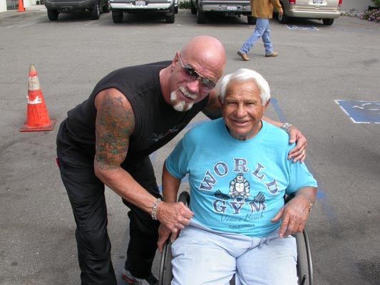 Joe Gold sitting in a wheelchair and posing for a photo with Ric Drasin