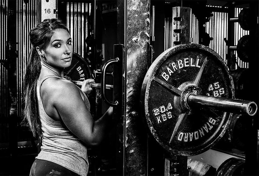 Karina Baymiller in a photo shoot next to a barbell rack.