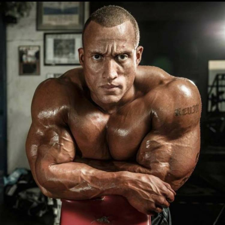 Kevin Jordan being shirtless, looking straight into the camera with a serious look on his face, looking big and muscular