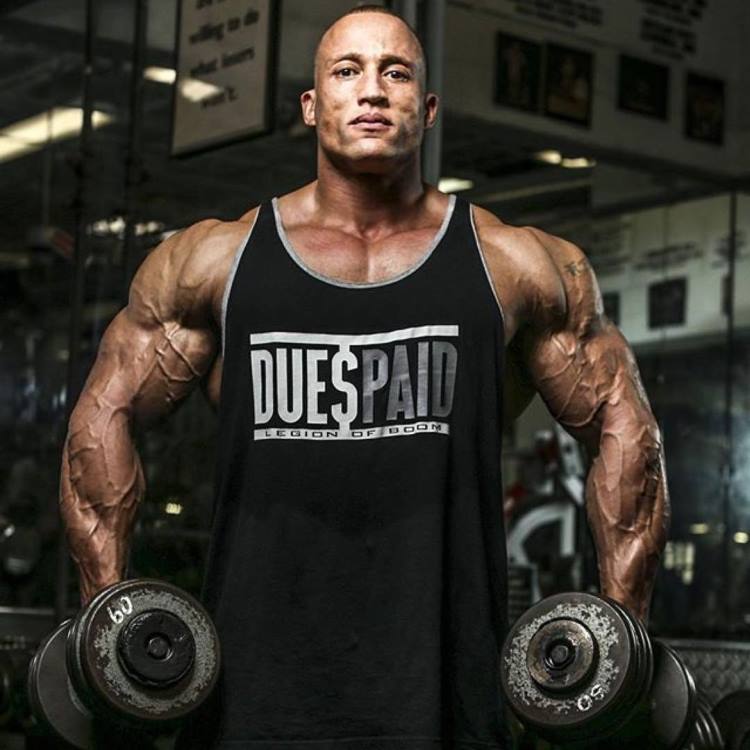 Kevin Jordan posing for a photo in a black tank top and two dumbbells in his hands