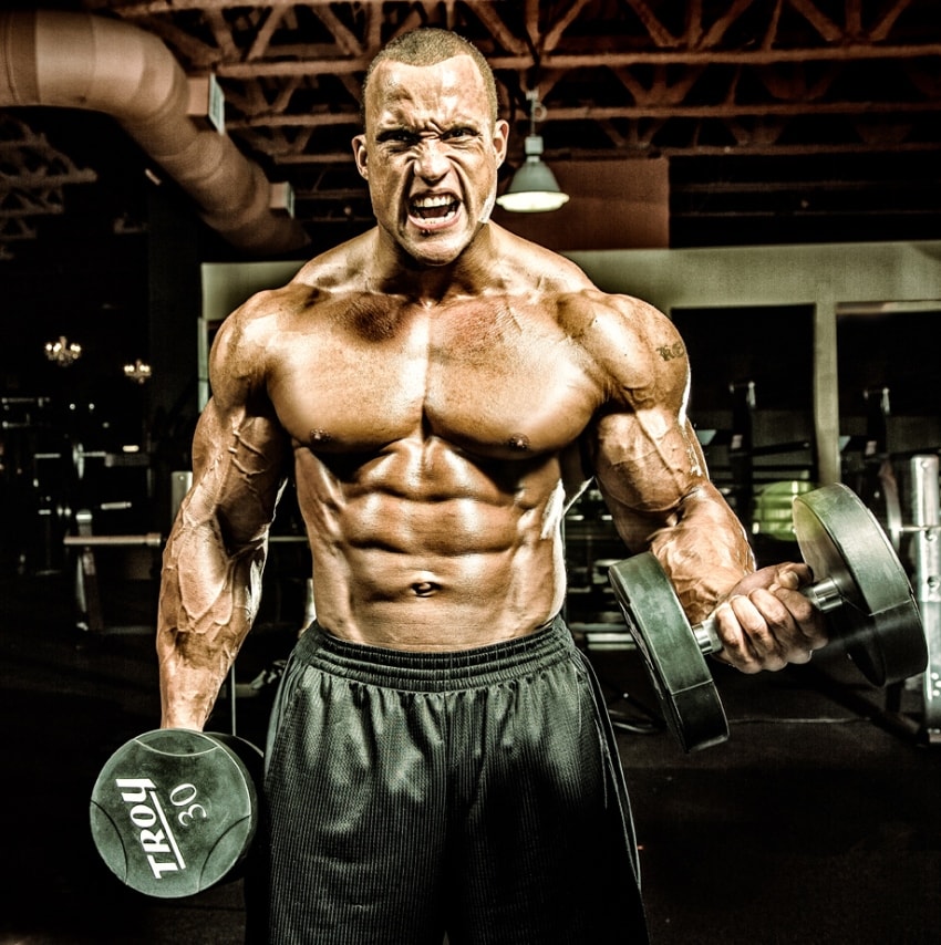 Kevin Jordan lifting heavy dumbbells while being shirtless in a gym
