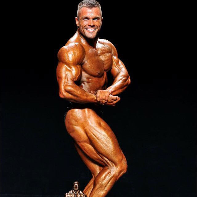 Mike Johnson flexing his bicep on the bodybuilding stage.