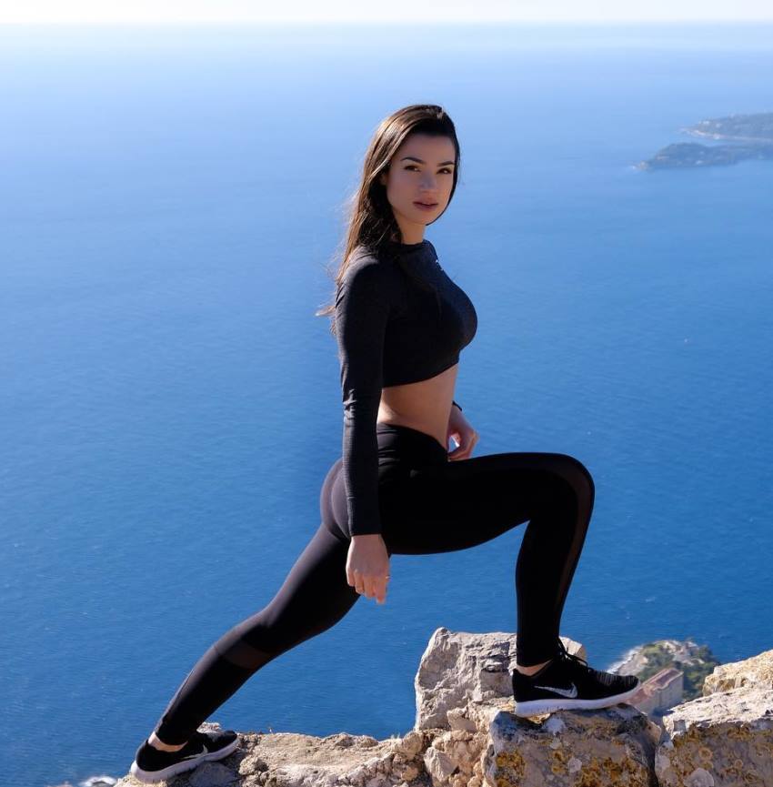 Sissy Mua doing lunges on a cliff overlooking a vast blue sea