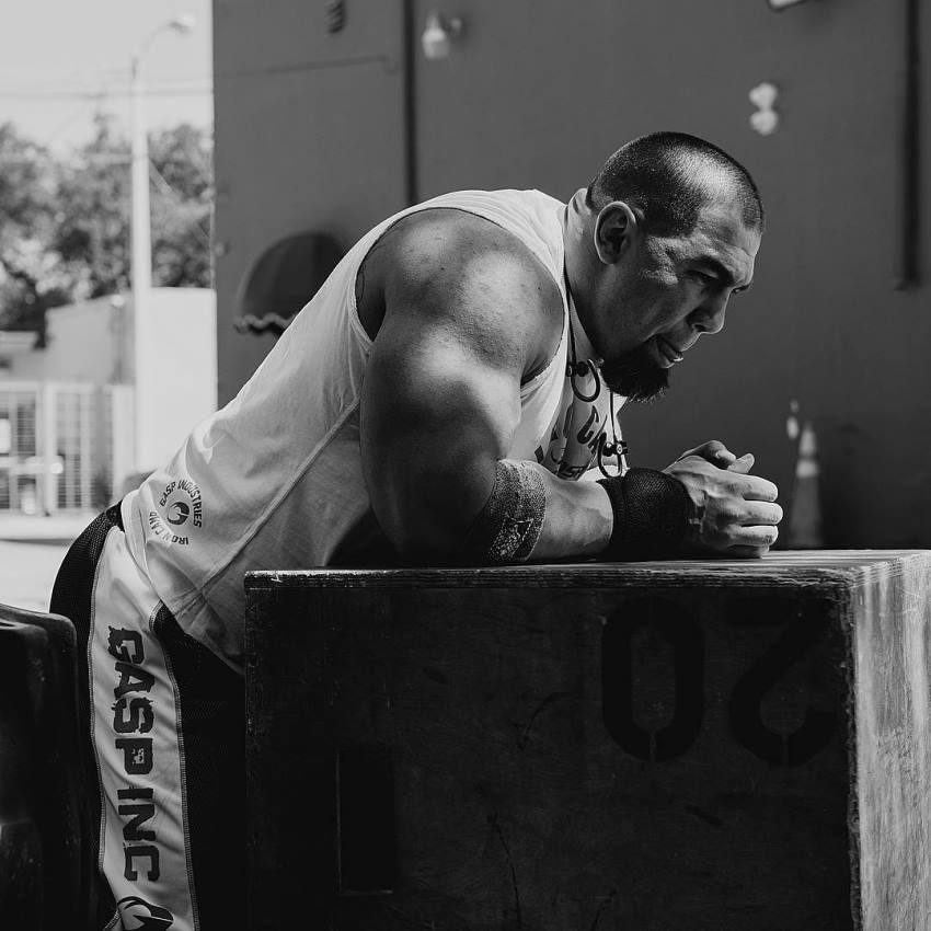 Tony Sentmanat leaning against an object showing off his massive and ripped arms