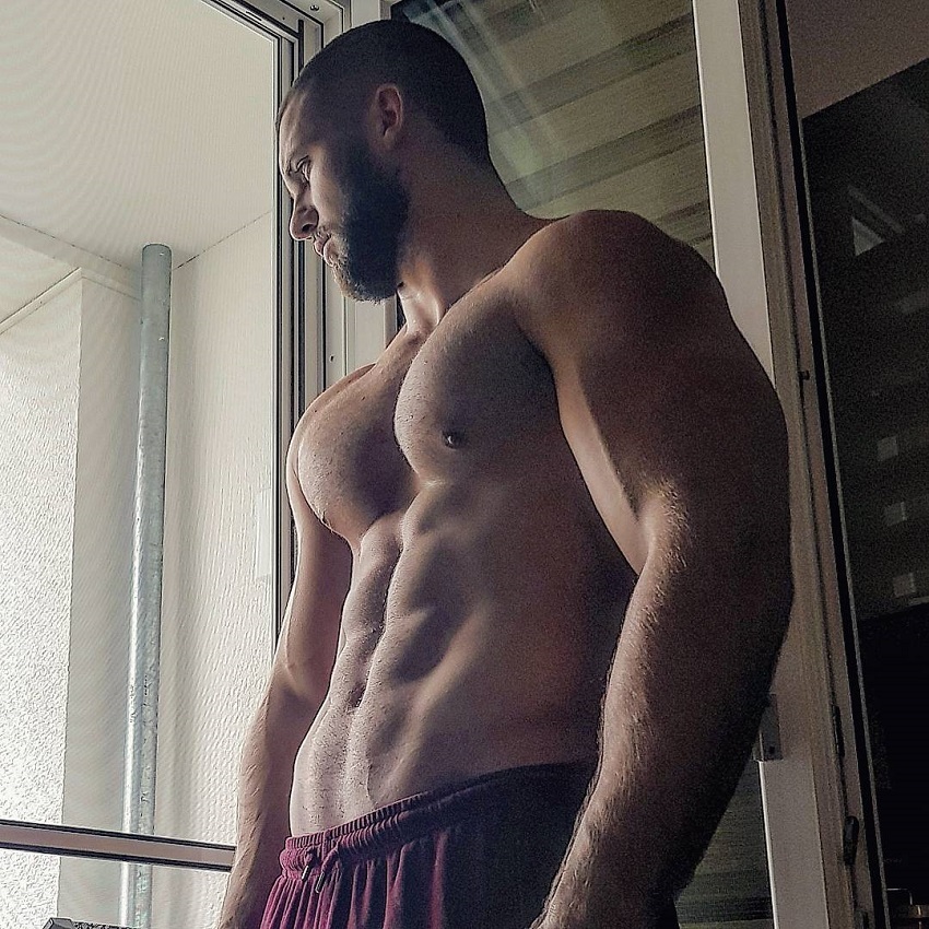 Florian Munteanu standing by the balcony without a shirt looking ripped and muscular