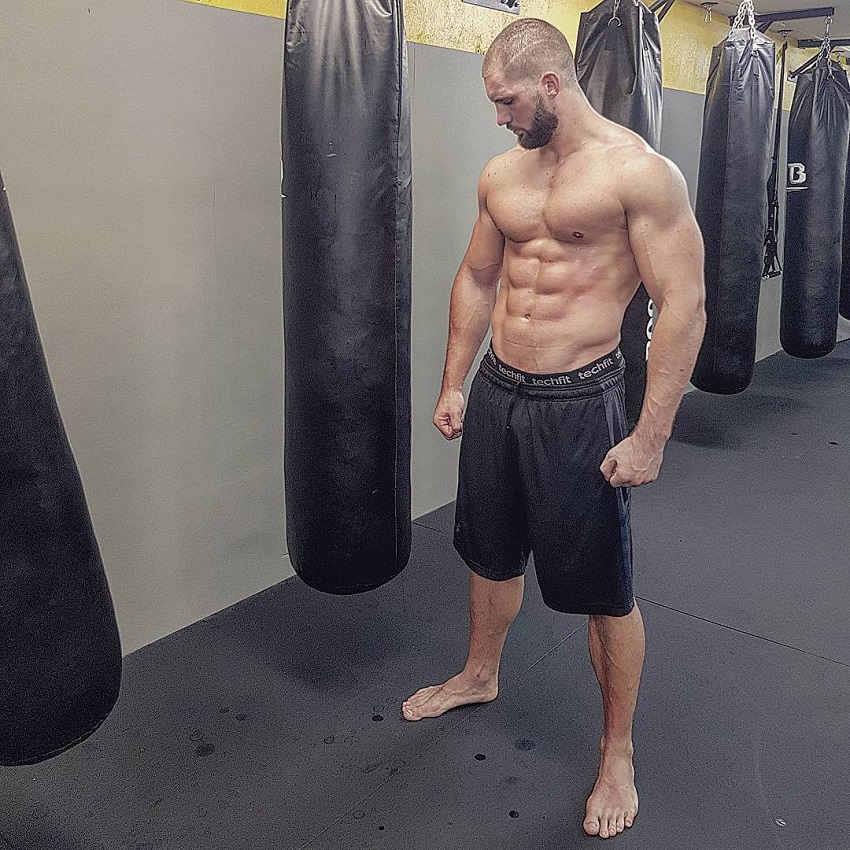 Florian Munteanu standing shirtless by a boxing bag looking big and lean