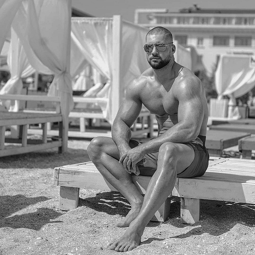 Florian Munteanu sitting shirtless on a beach looking fit and lean